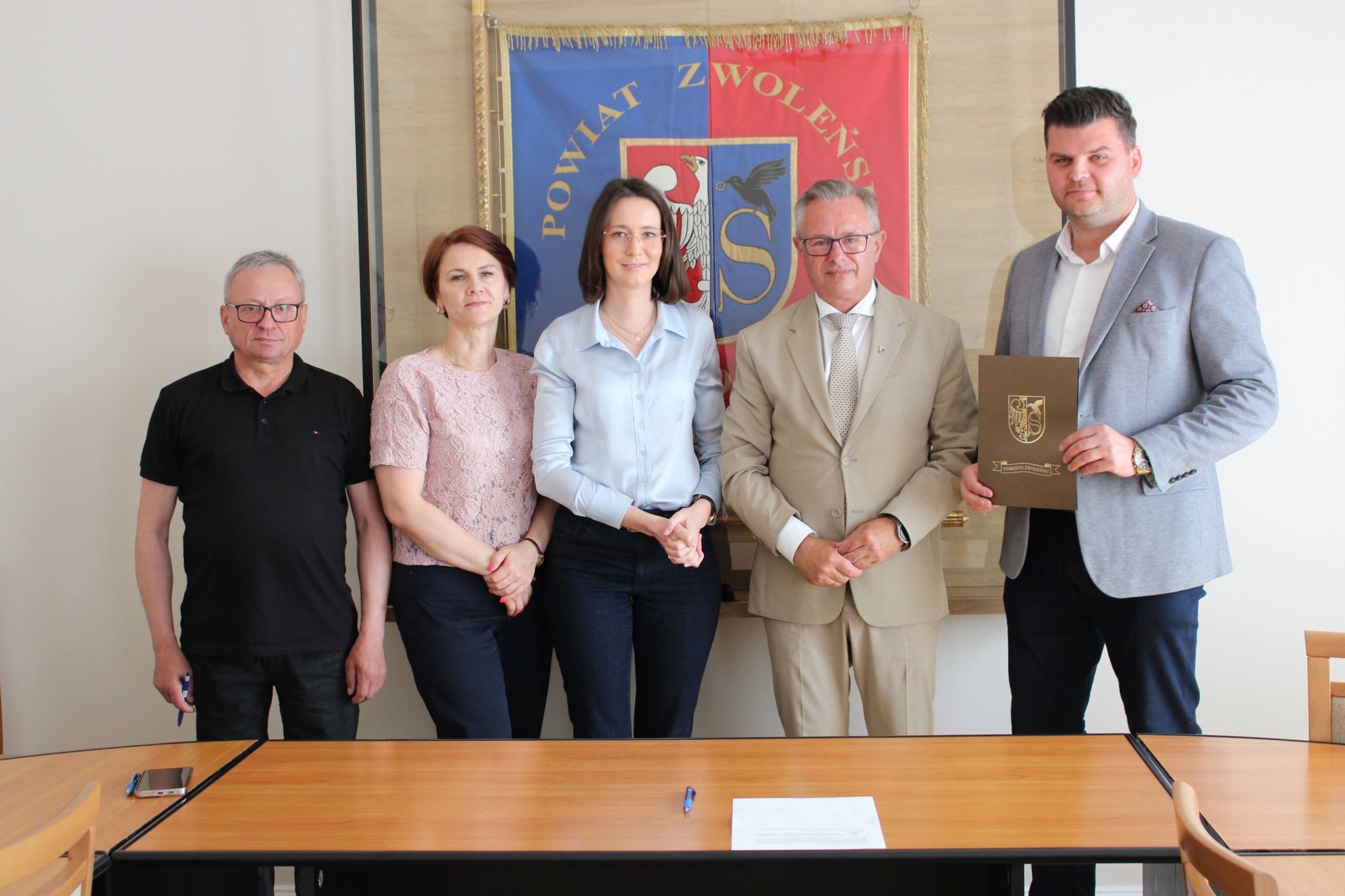 Zdjęcie przedstawia grupę os&oacute;b stojących na tle sztandaru powiatu zwoleńskiego.