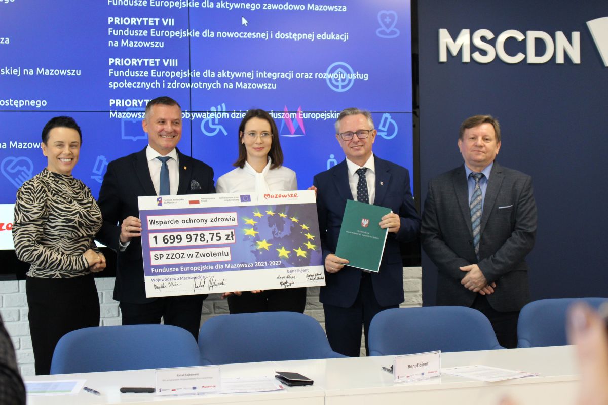 Zdjęcie przedstawia grupę osób stojących na podeście z symbolicznym czekiem.