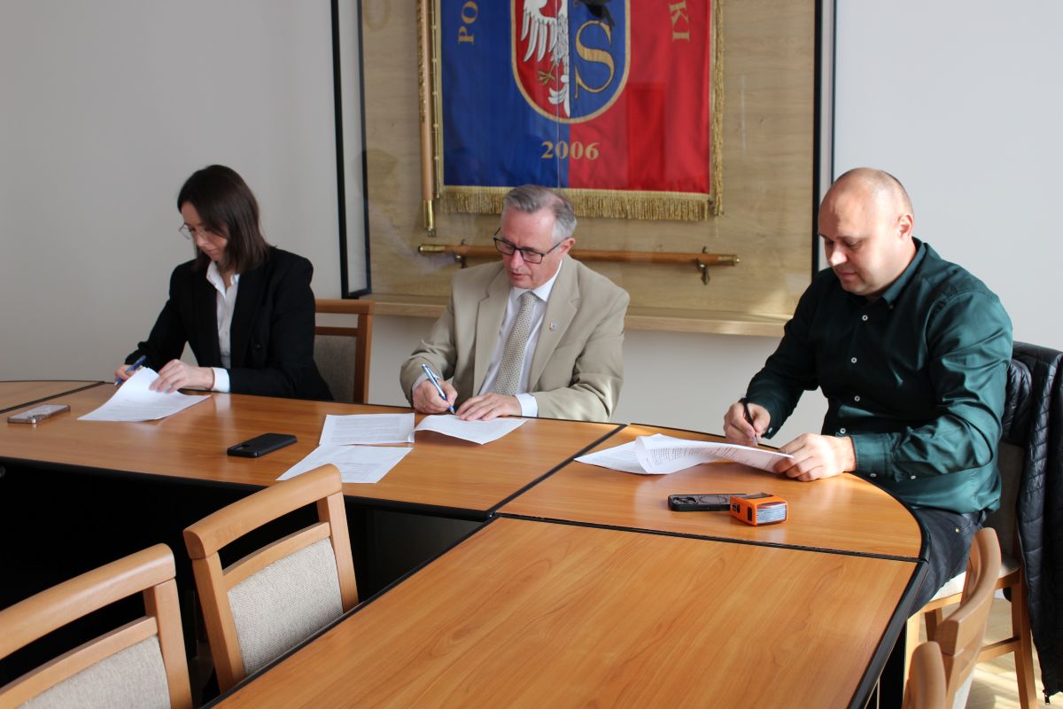 Zdjęcie przedstawia 3 osoby podpisujące umowę.