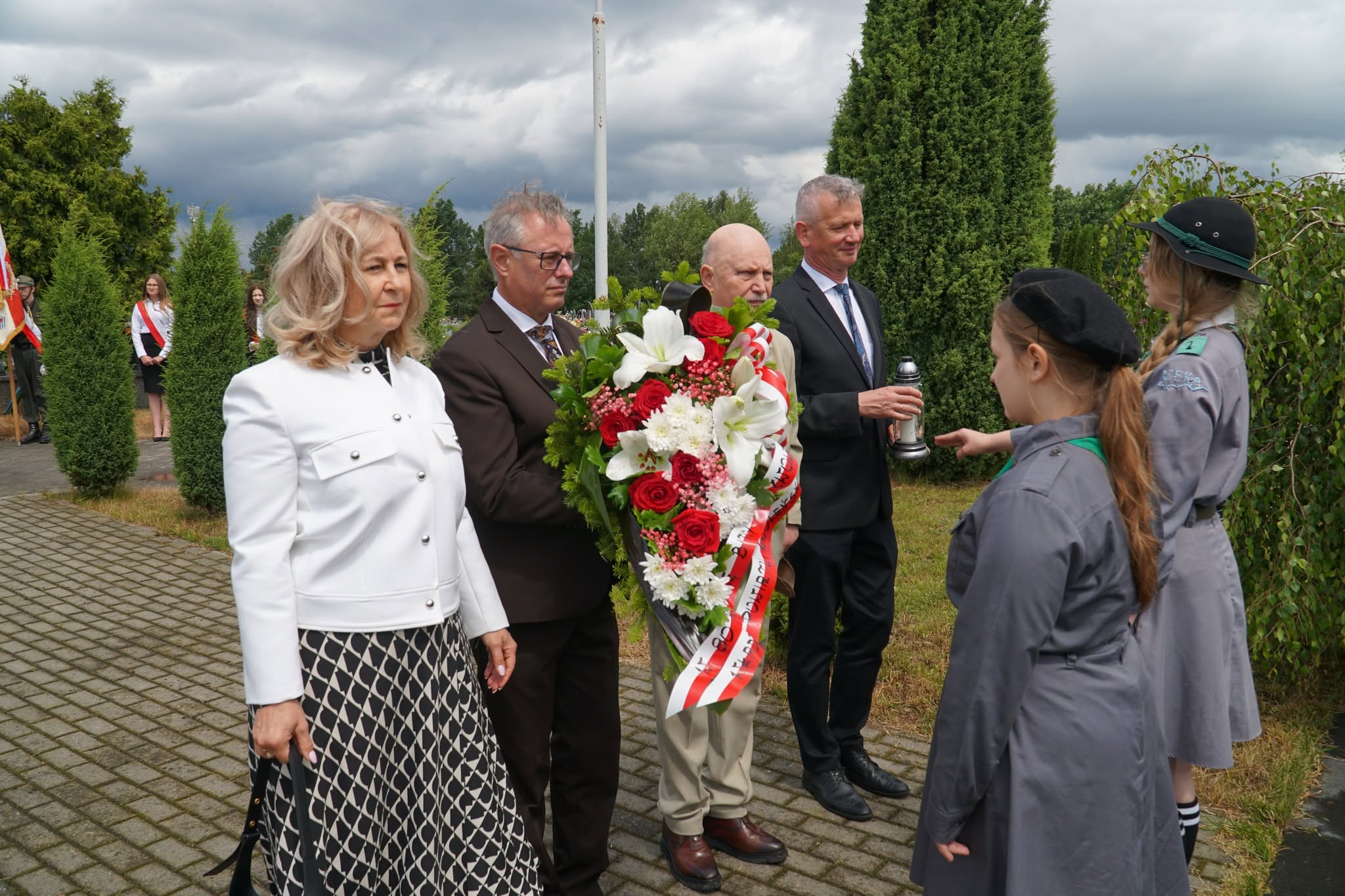 Zdjęcie przedstawia grupę os&oacute;b składających wiązankę pod pomnikiem na cmentarzu w Zwoleniu.